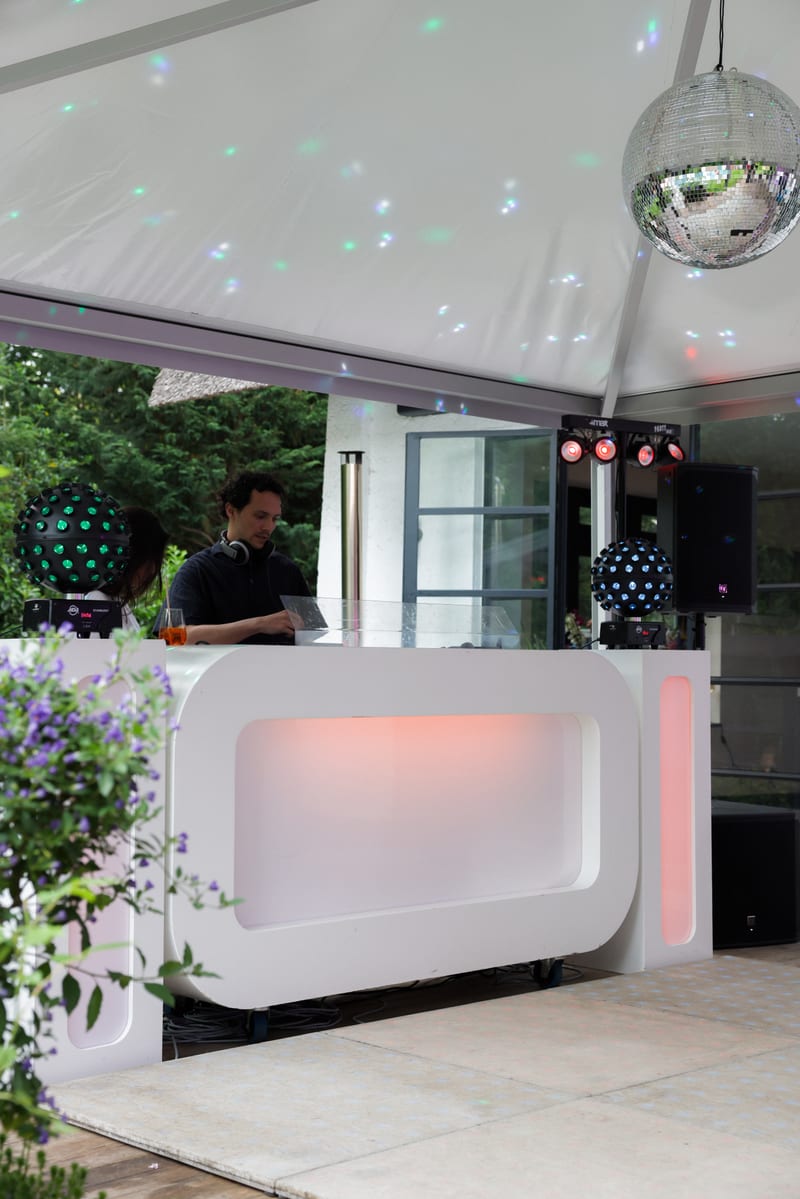 DJ achter een witte booth in een tuintent