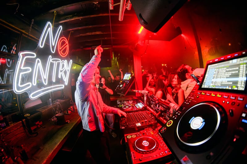 DJ in rood licht onder een neonbord tijdens een clubnacht